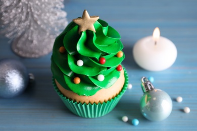 Photo of Christmas tree shaped cupcake and decor on light blue wooden table, closeup