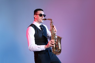 Photo of Young man in elegant outfit playing saxophone on color background
