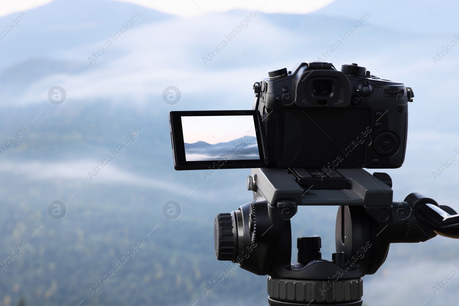 Photo of Taking video with modern camera on tripod in mountains