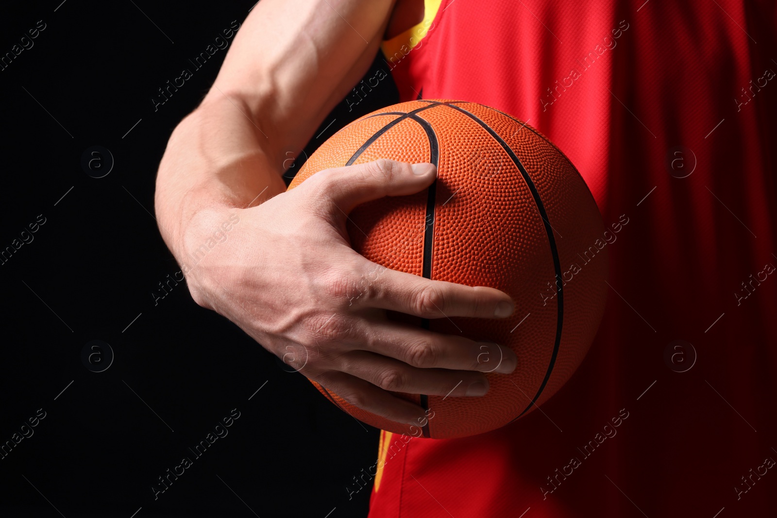 Photo of Athletic man with basketball ball on black background, closeup