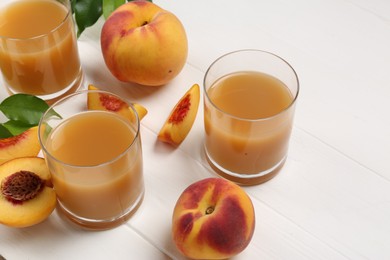 Glasses of peach juice, fresh fruits and leaves on white wooden table