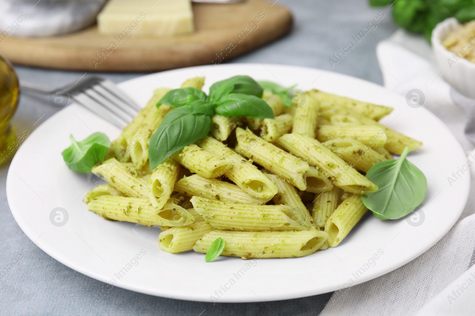 Photo of Delicious pasta with pesto sauce and basil on light grey table, closeup