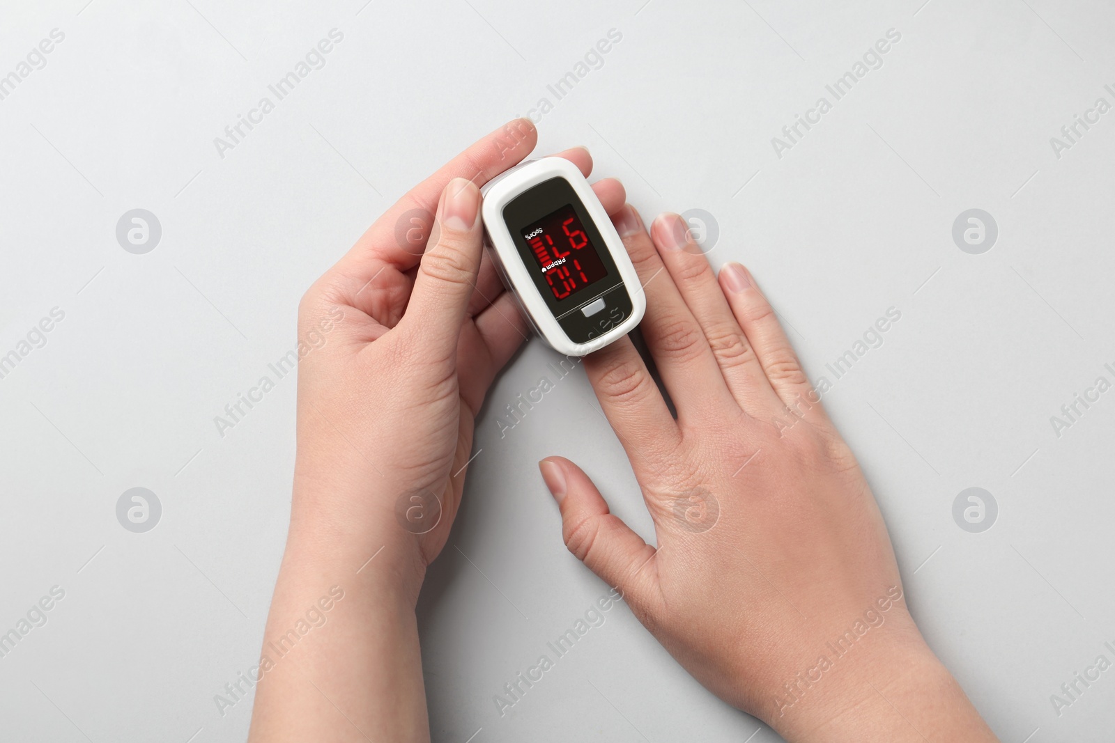 Photo of Woman using fingertip pulse oximeter on white background, top view