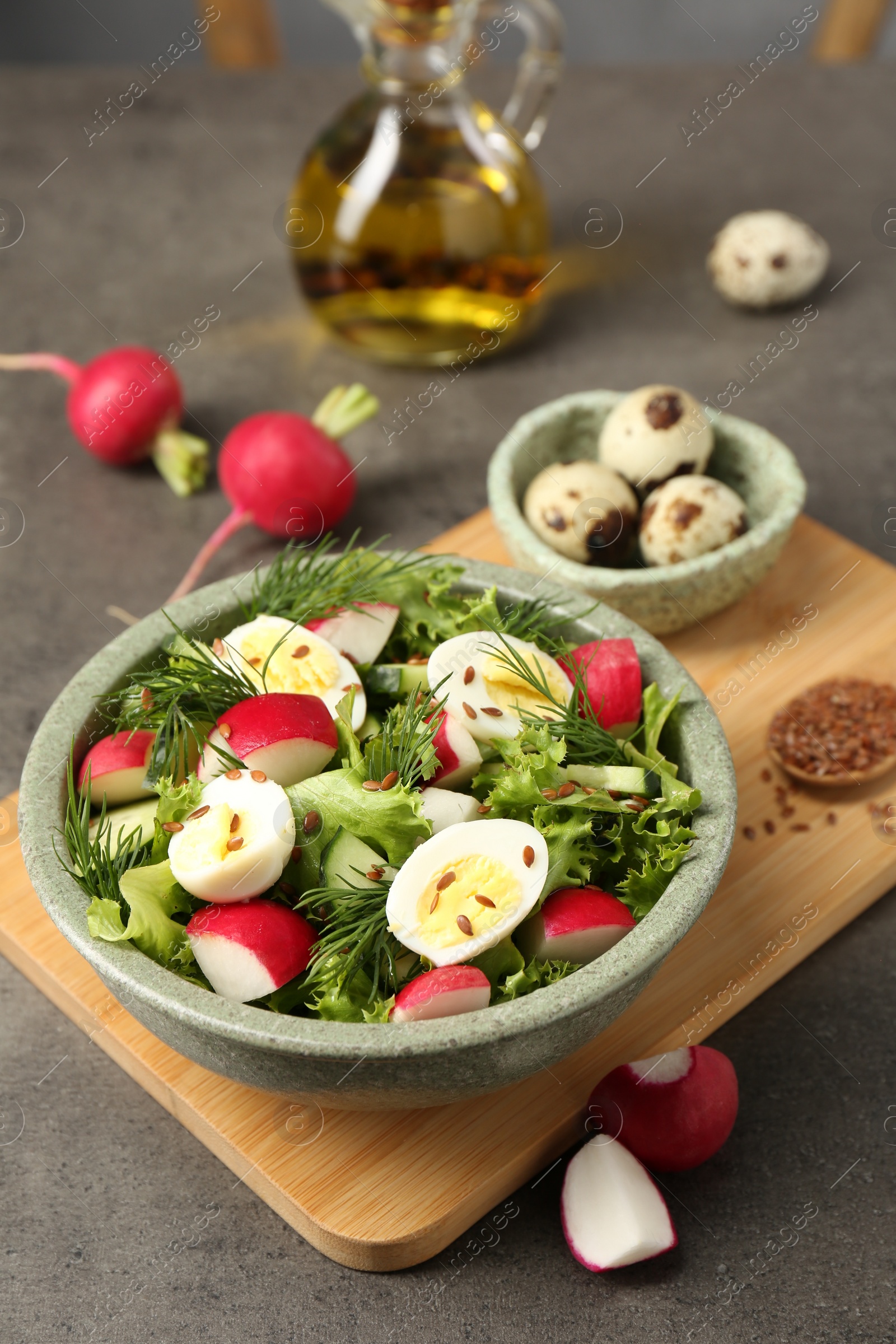 Photo of Delicious salad with radish, lettuce and boiled quail eggs on grey table