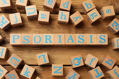 Photo of Word Psoriasis made of cubes with letters on wooden table, flat lay