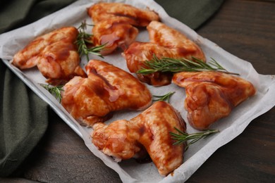 Photo of Raw marinated chicken wings and rosemary on wooden table, closeup