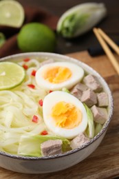 Photo of Bowl of delicious rice noodle soup with meat and egg on wooden board, closeup