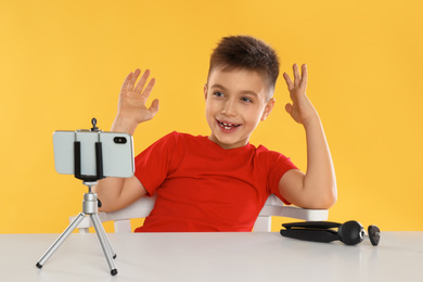 Cute little blogger recording video at table on yellow background
