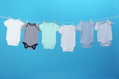 Photo of Colorful baby onesies hanging on clothes line against blue background. Laundry day