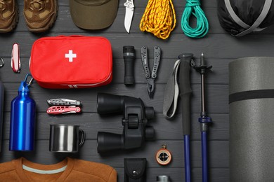 Photo of Flat lay composition with trekking poles and other hiking equipment on dark grey wooden background