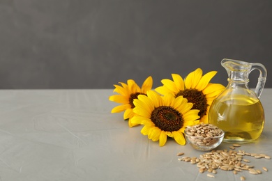 Photo of Sunflowers, jug of oil and seeds on grey table, space for text