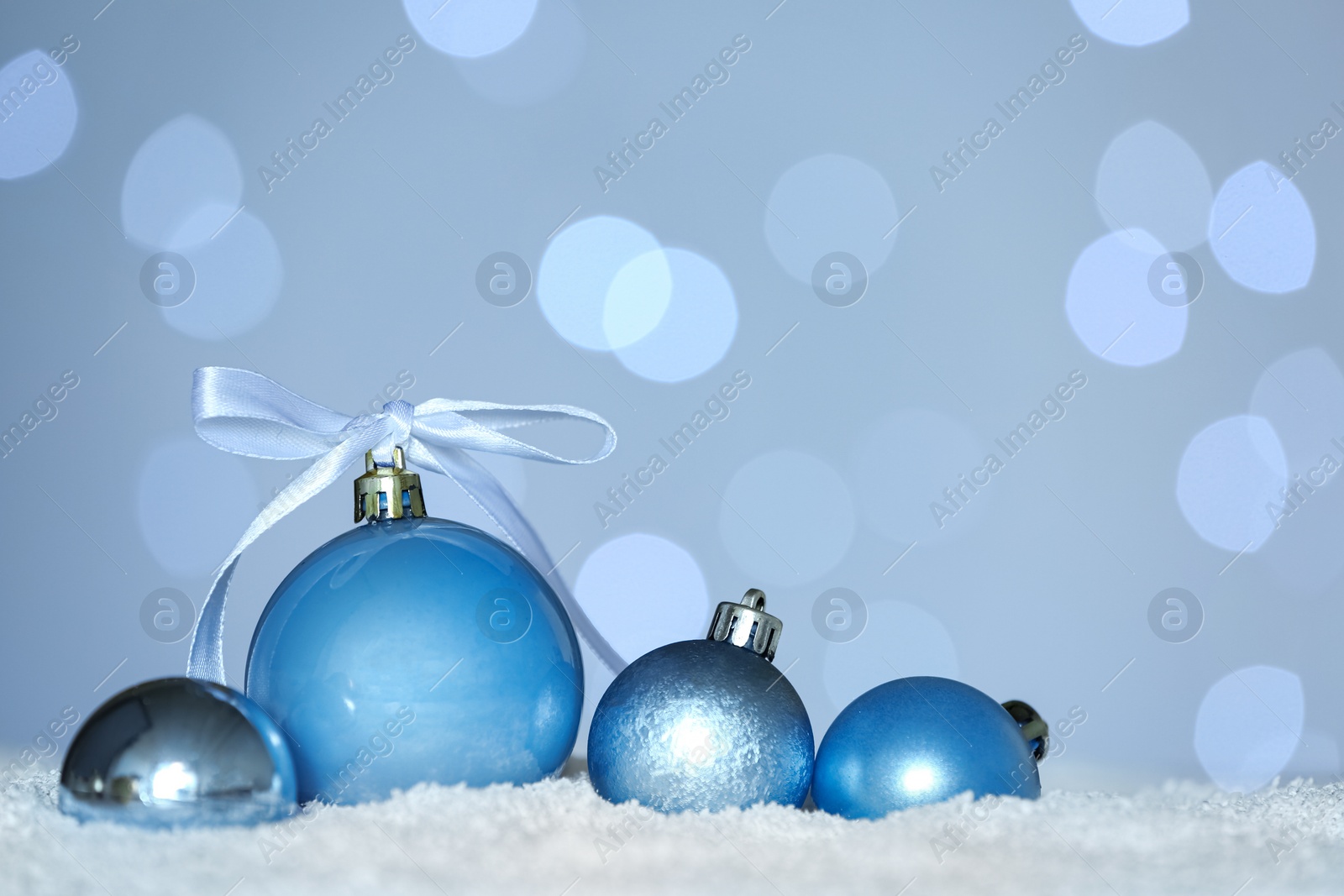 Photo of Beautiful light blue Christmas balls on snow against blurred festive lights. Space for text