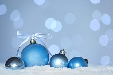 Beautiful light blue Christmas balls on snow against blurred festive lights. Space for text