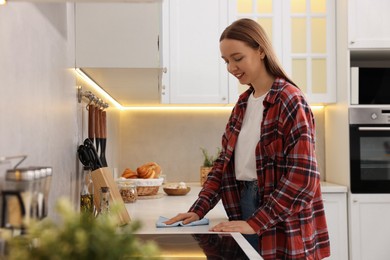 Photo of Woman with microfiber cloth cleaning white marble countertop in kitchen