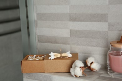 Cotton swabs and flowers on tiled surface in bathroom