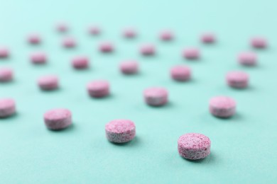 Photo of Many pink vitamin pills on turquoise background, closeup
