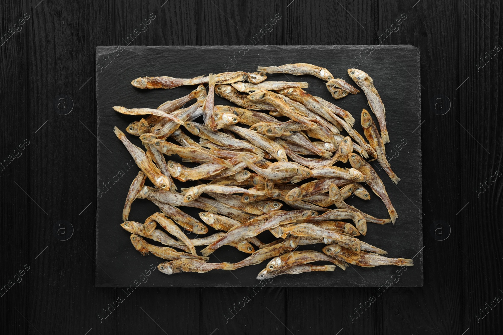 Photo of Delicious dried anchovies on black wooden table, top view