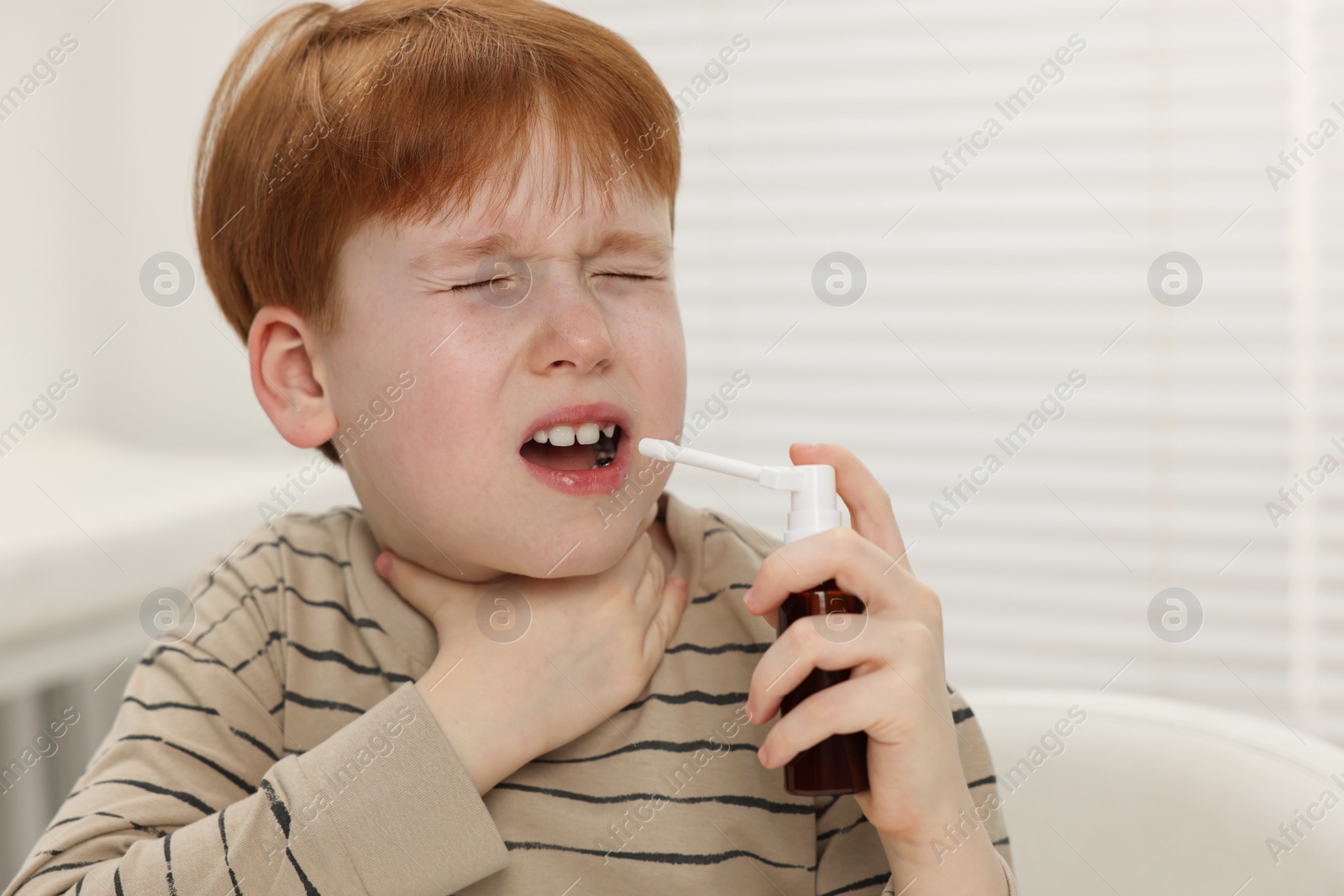 Photo of Little boy using throat spray at home