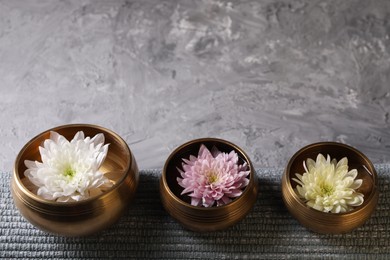 Photo of Tibetan singing bowls with water, beautiful chrysanthemum flowers on grey textured table. Space for text