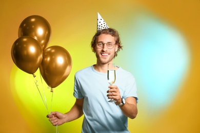 Portrait of happy man with champagne in glass and party balloons on color background