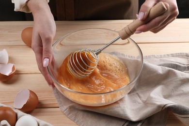 Woman whisking eggs in bowl at table, closeup