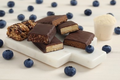 Photo of Different energy bars, blueberries and protein powder on white wooden table, closeup