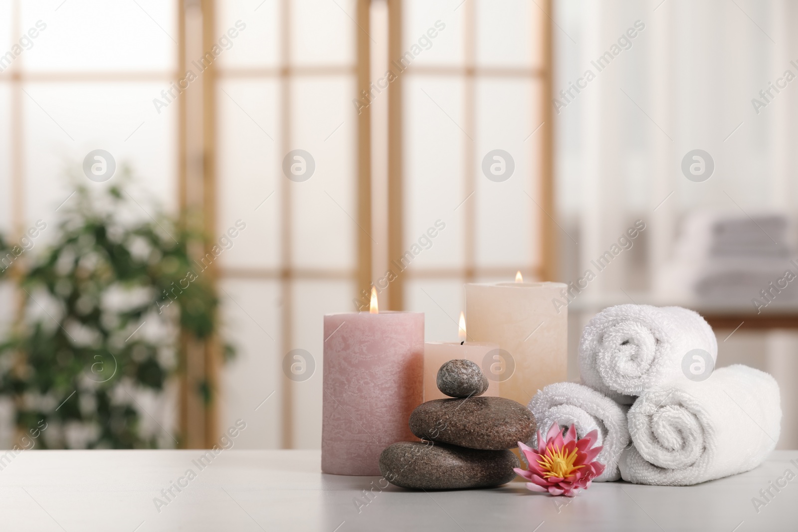 Photo of Spa composition. Burning candles, lotus flower, stones and towels on white table indoors, space for text