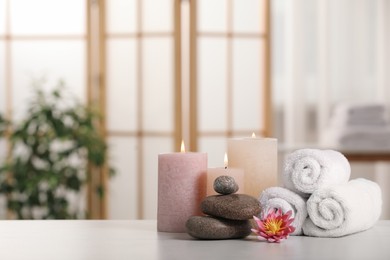 Photo of Spa composition. Burning candles, lotus flower, stones and towels on white table indoors, space for text