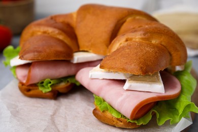 Photo of Tasty crescent roll with brie, ham and lettuce on parchment paper, closeup