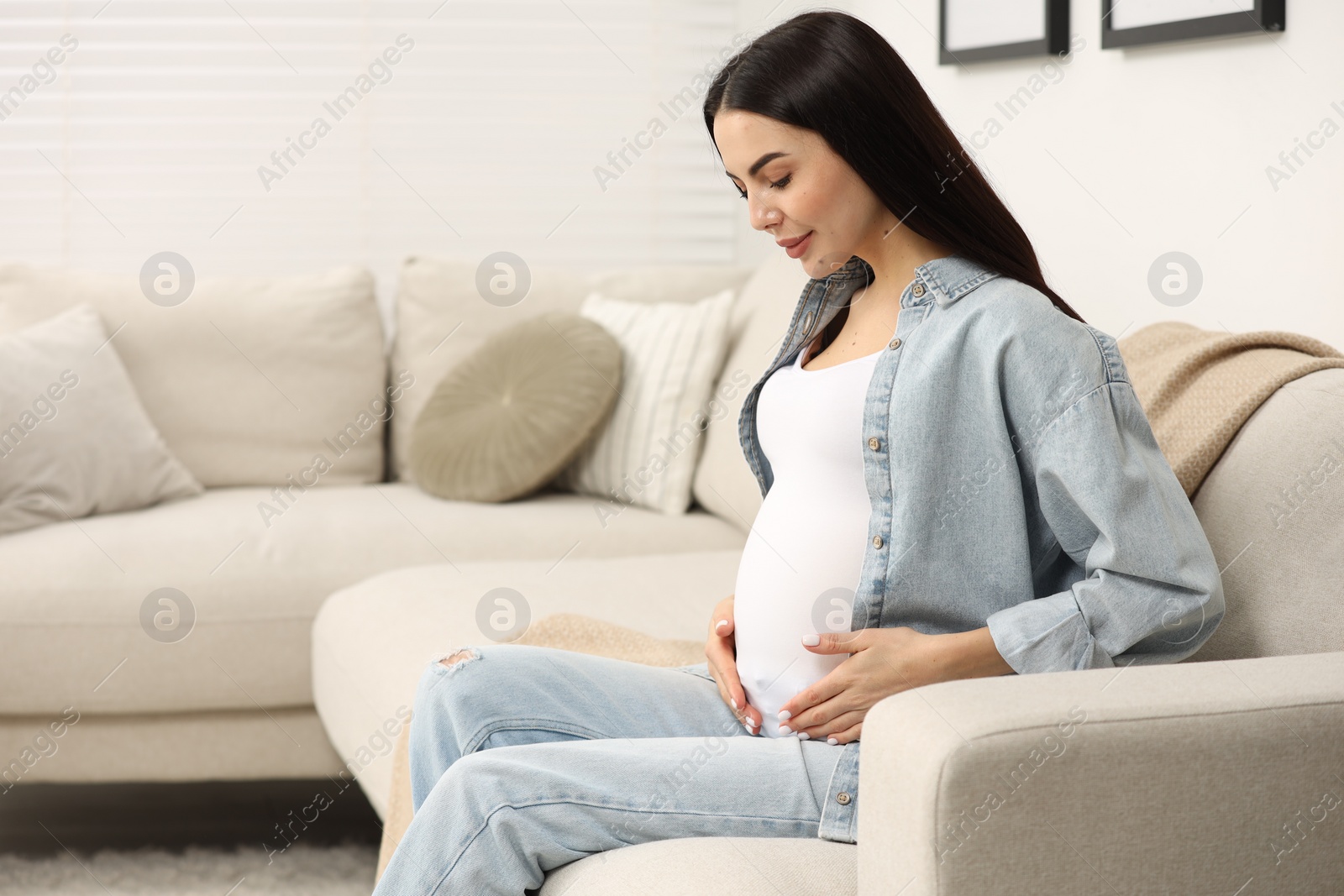 Photo of Pregnant young woman on sofa at home, space for text