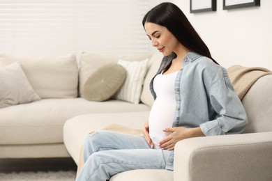 Pregnant young woman on sofa at home, space for text