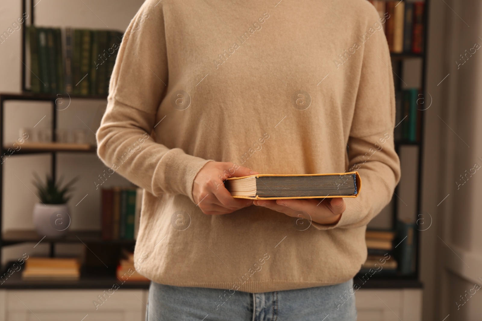 Photo of Young woman reading book in home library, closeup