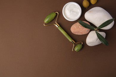 Flat lay composition with jar of cream, face roller and stones on brown background. Space for text