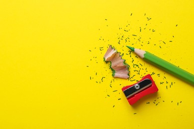 Photo of Green pencil, wooden shavings, crumbs and sharpener on yellow background, flat lay. Space for text
