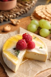 Photo of Brie cheese served with berries and honey on wooden board, closeup