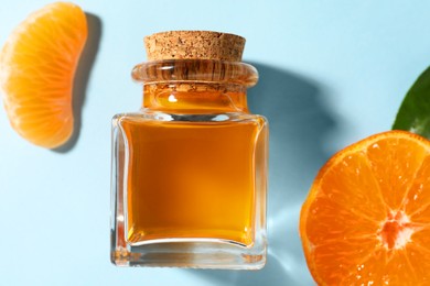 Photo of Aromatic tangerine essential oil in bottle and citrus fruit on light blue table, top view