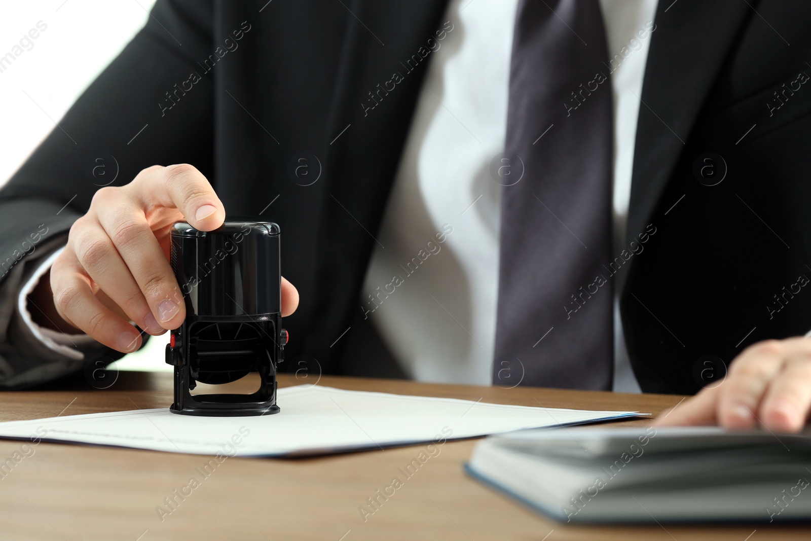 Photo of Male notary stamping document at table, closeup