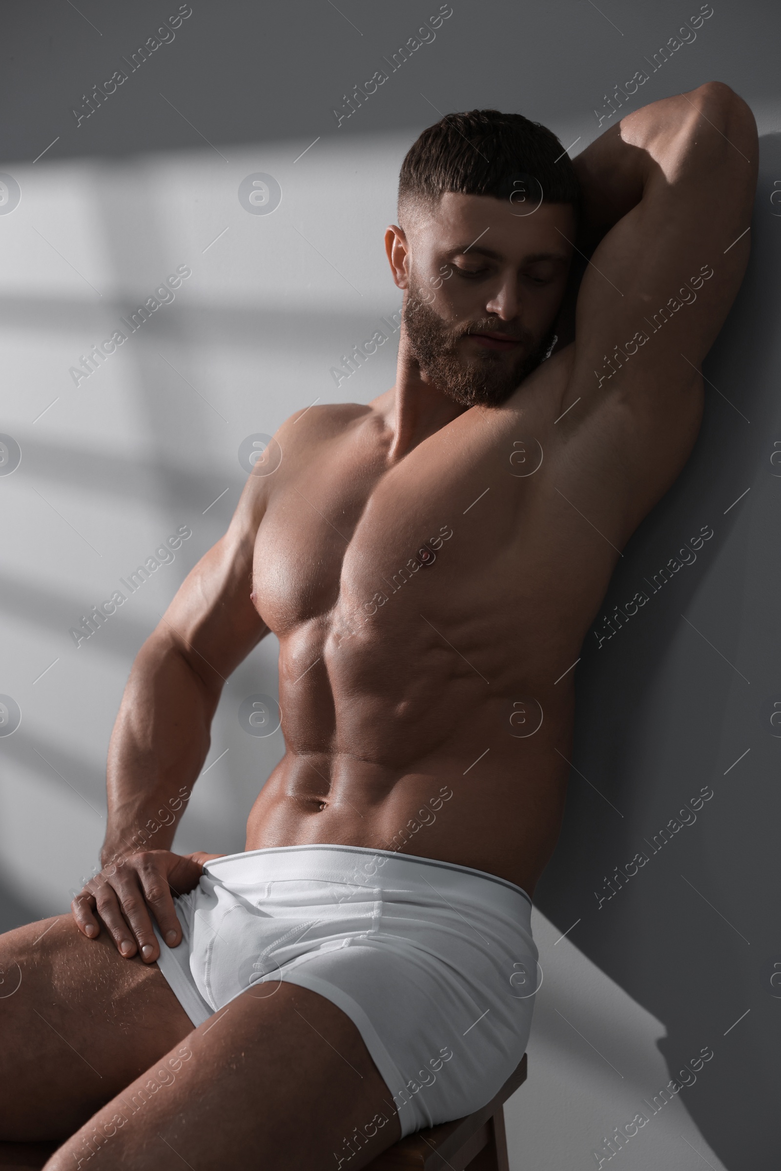 Photo of Young man in stylish white underwear sitting on chair near grey wall