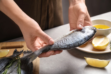 Woman holding dorada fish over grey table, closeup