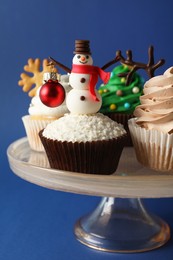 Dessert stand with tasty Christmas cupcakes on blue background