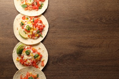 Photo of Delicious tacos with vegetables and lime on wooden table, top view. Space for text