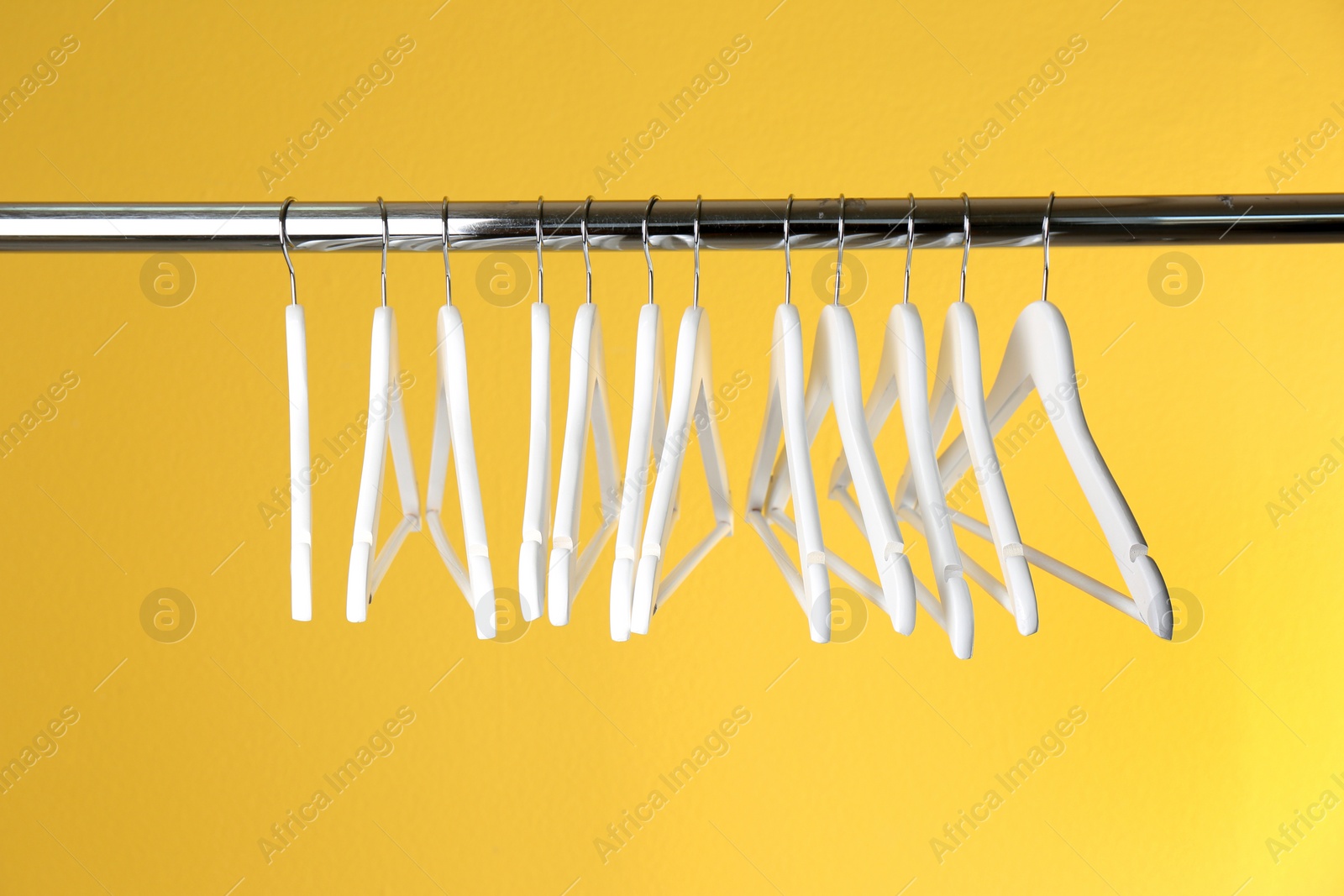 Photo of Metal rack with clothes hangers on color background