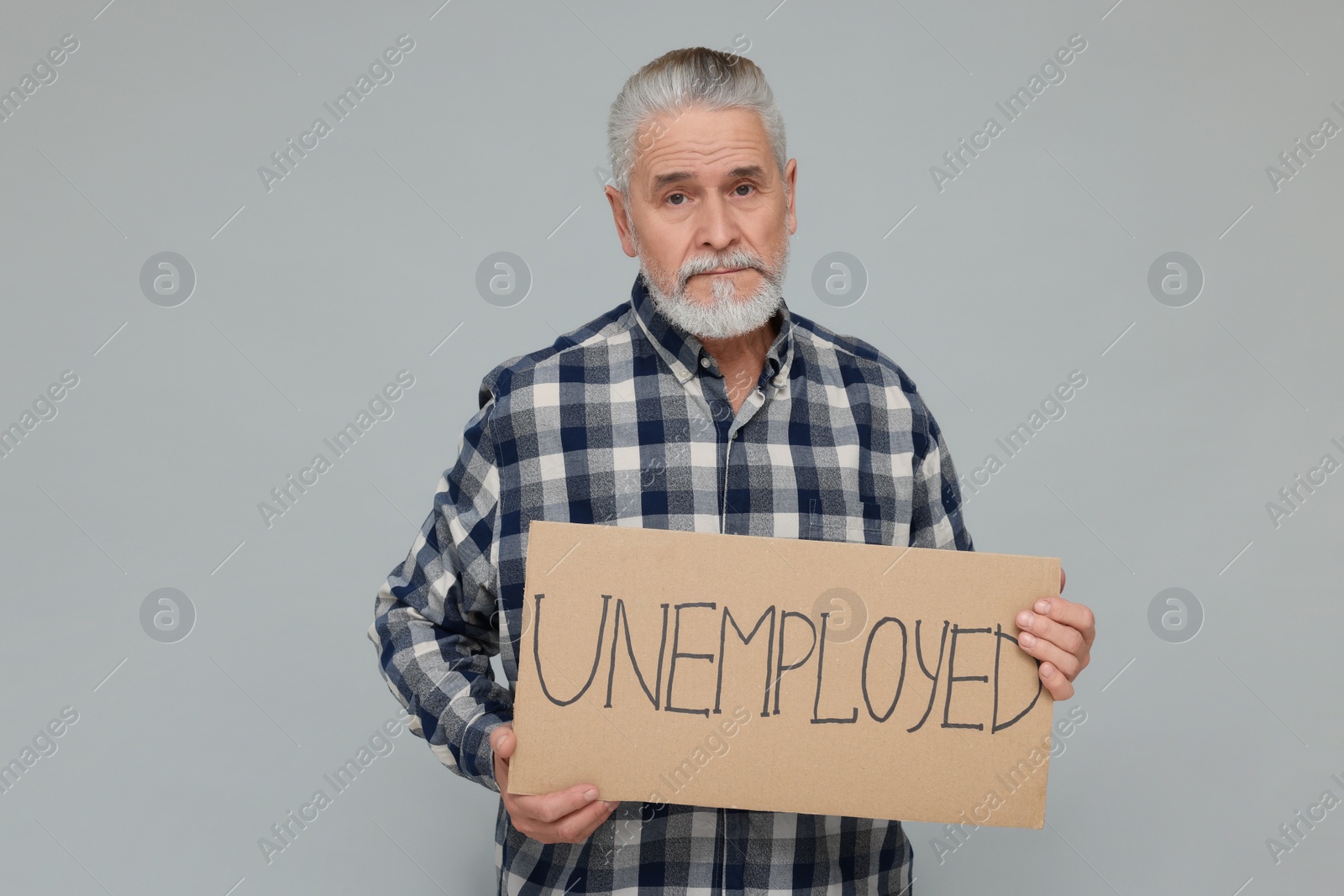 Photo of Senior man holding cardboard sign with word Unemployed on light grey background