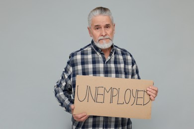 Senior man holding cardboard sign with word Unemployed on light grey background