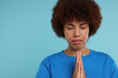 Photo of Woman with clasped hands praying to God on light blue background. Space for text