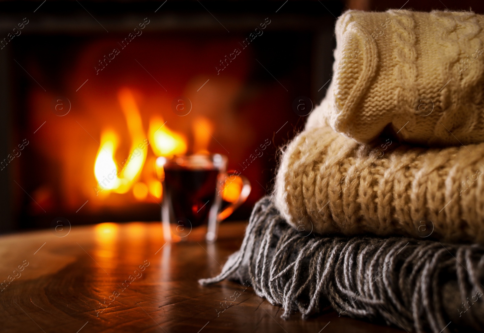 Photo of Stack of knitted clothes and blurred fireplace on background