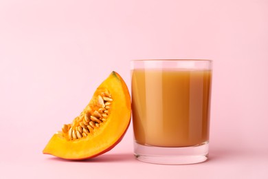 Tasty pumpkin juice in glass and cut pumpkin on pink background