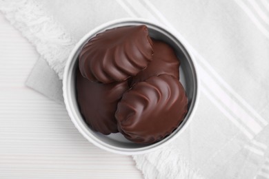 Photo of Delicious chocolate covered zephyrs in bowl on white wooden table, top view