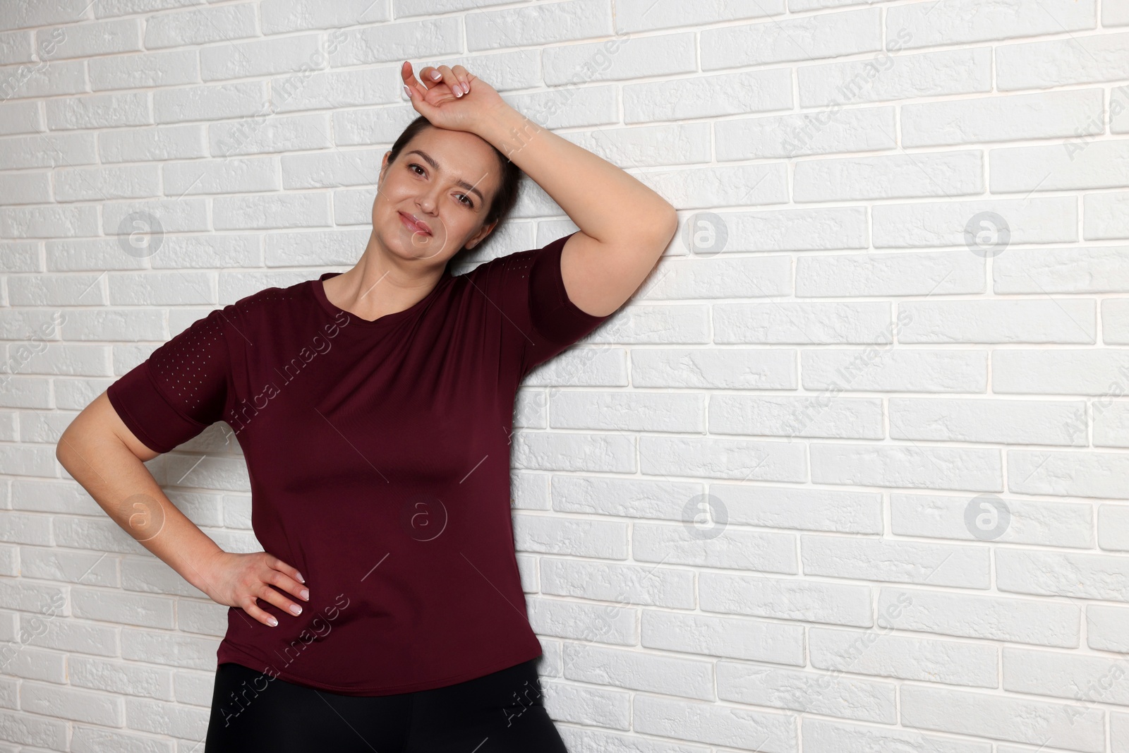 Photo of Happy overweight woman near white brick wall, space for text