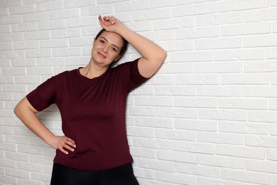 Happy overweight woman near white brick wall, space for text
